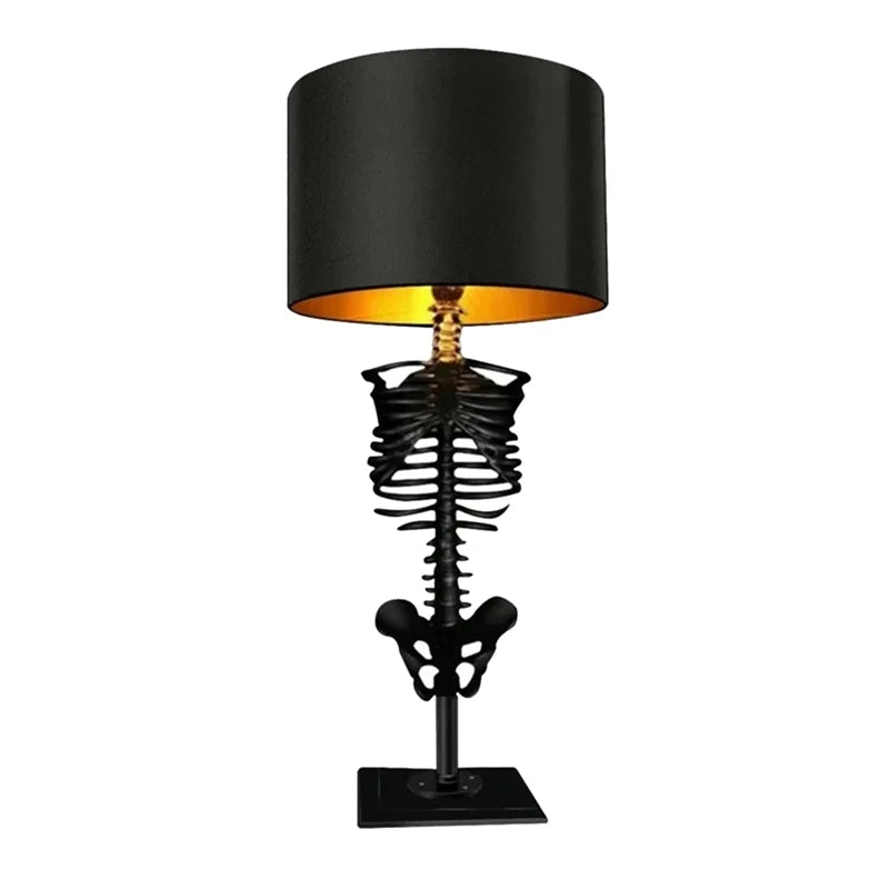 Gothic table lamp built on a black skeleton torso and ribcage, topped with a black drum shade with a warm gold interior lining.