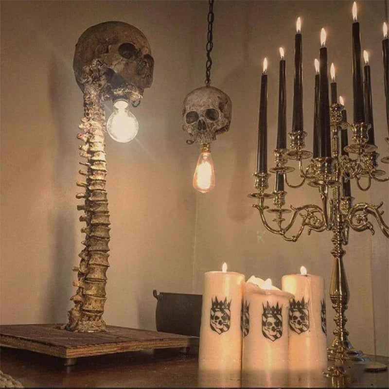 A small desk lamp built as a skull sitting atop a full vertebral column, finished in an aged, bone-toned resin.