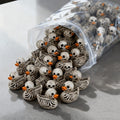 A collection of tiny bone-white skeleton duck resin figurines with orange beaks and skull detailing, shown spilling from a clear plastic bag.