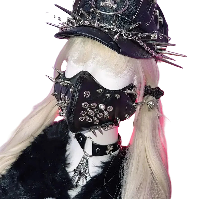 A gothic punk-style black faux-leather mask with spikes and rhinestones, shown on a mannequin with a matching spiked hat, collar, and long blonde pigtails against a pink and purple background.